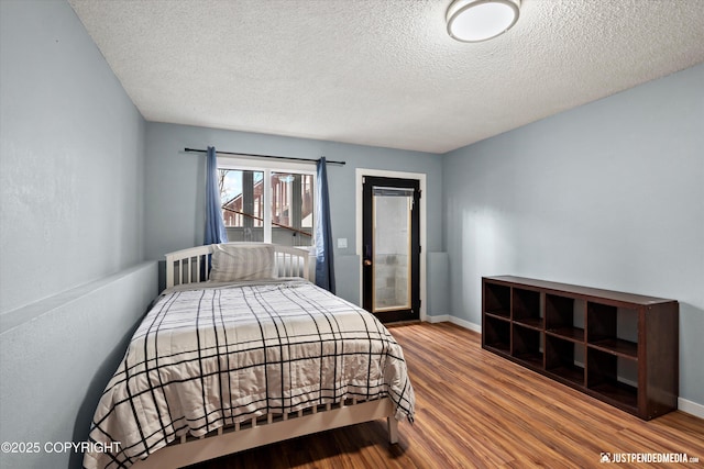 bedroom with wood finished floors, a textured ceiling, access to outside, and baseboards