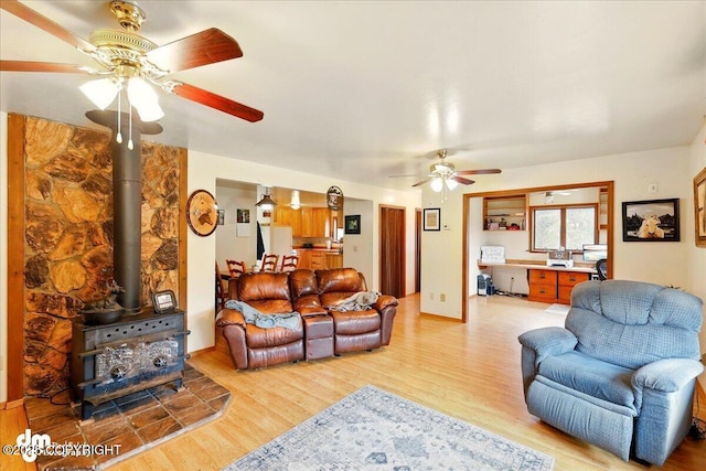 living area with ceiling fan, light wood-style flooring, a wood stove, and an office area