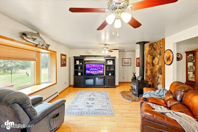 living room featuring a baseboard heating unit, wood finished floors, a wood stove, and ceiling fan