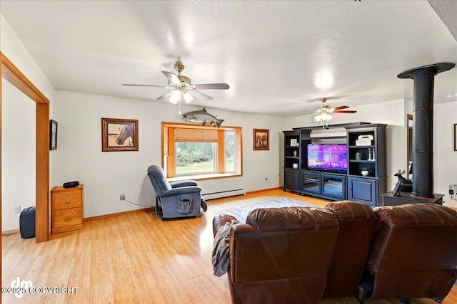 living room with a baseboard radiator, a ceiling fan, wood finished floors, a wood stove, and baseboards