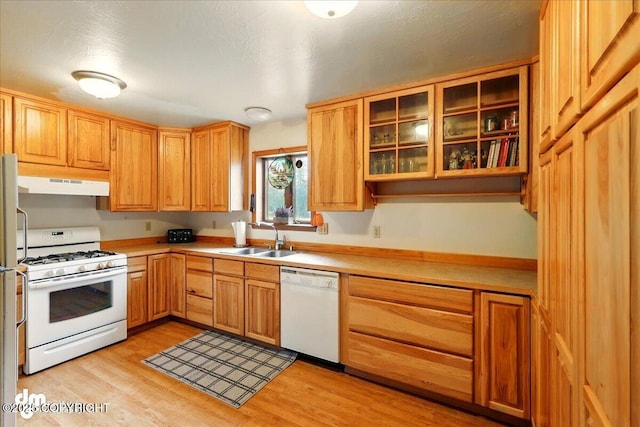 kitchen featuring white appliances, a sink, under cabinet range hood, and light countertops