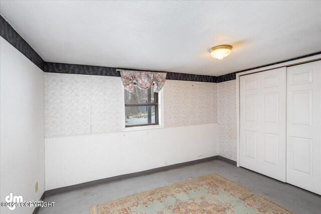 3669 Pullen Cir, Eagle River, AK 99577 - unfurnished bedroom featuring concrete flooring, baseboards, a wainscoted wall, a closet, and wallpapered walls