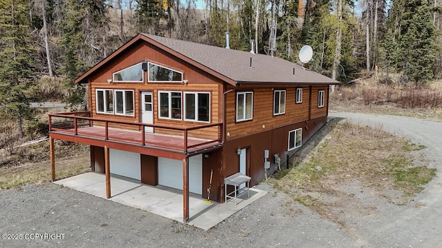 575 Pace St, Soldotna, AK 99669 - rear view of house featuring dirt driveway, a garage, a shingled roof, and a deck