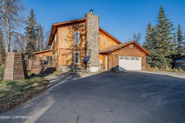 view of front facade with a chimney, aphalt driveway, a wooden deck, and an attached garage