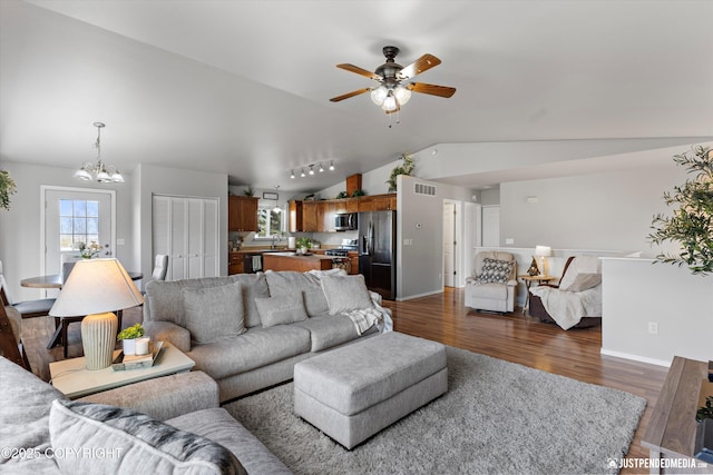 living area with dark wood-style flooring, visible vents, lofted ceiling, and ceiling fan with notable chandelier