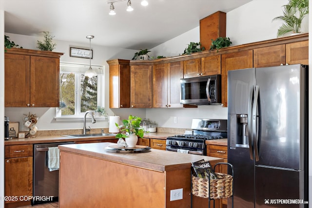 kitchen with pendant lighting, appliances with stainless steel finishes, a center island, a sink, and light countertops