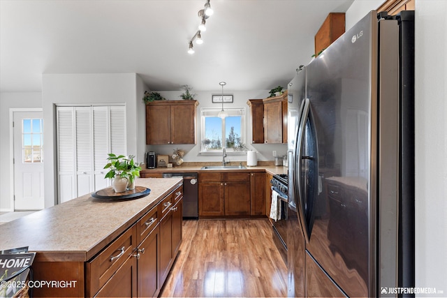 kitchen with a sink, appliances with stainless steel finishes, brown cabinetry, and light wood-style floors