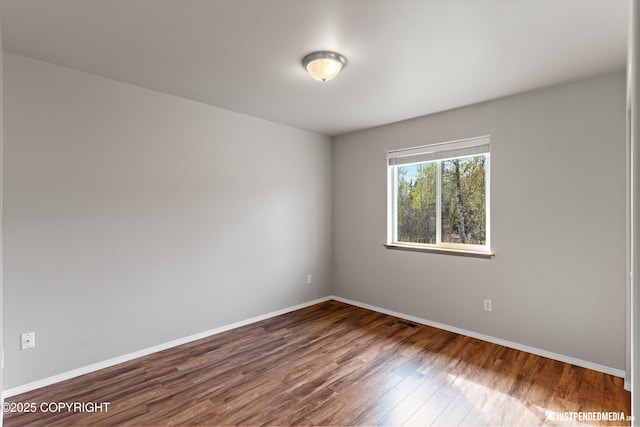 unfurnished room with baseboards, visible vents, and dark wood-type flooring