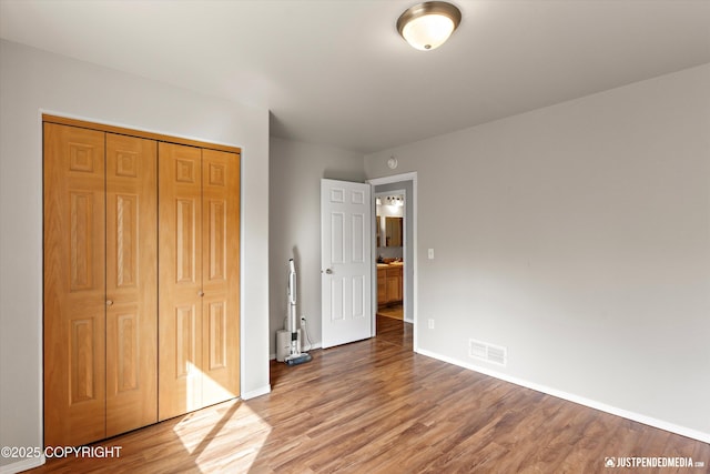unfurnished bedroom featuring baseboards, a closet, wood finished floors, and visible vents