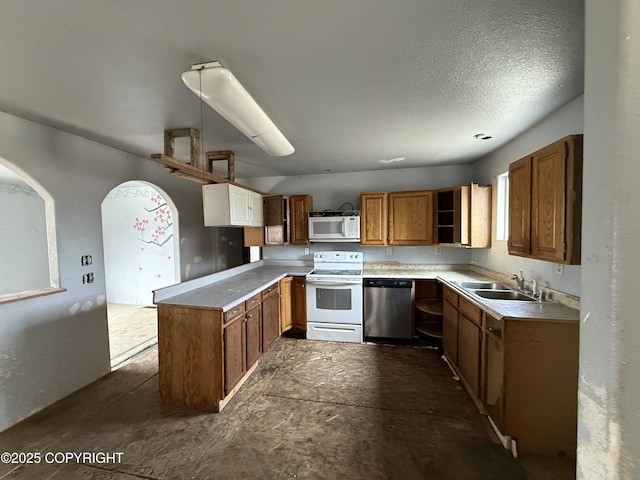 kitchen with a sink, white appliances, brown cabinetry, a peninsula, and light countertops