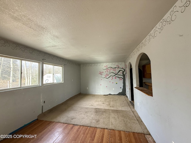 unfurnished room featuring a textured ceiling, wood finished floors, and arched walkways