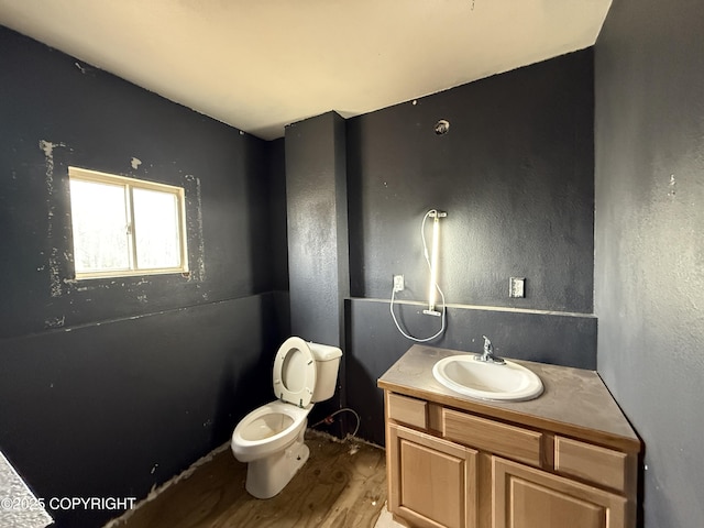 half bath with toilet, vanity, and wood finished floors