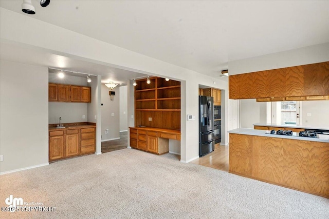 12100 Woodway Cir, Anchorage, AK 99516 - kitchen with black refrigerator with ice dispenser, light colored carpet, brown cabinetry, track lighting, and baseboards