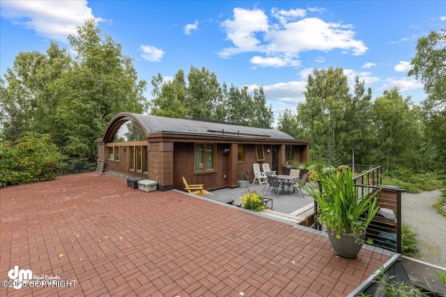 back of house with a patio, a deck, roof mounted solar panels, and outdoor dining area