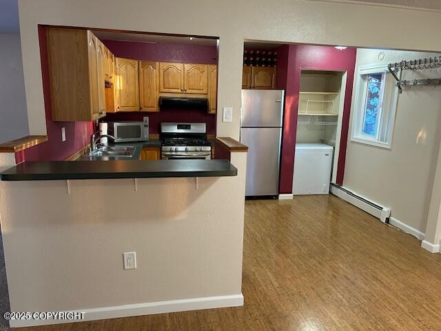 kitchen featuring appliances with stainless steel finishes, a baseboard radiator, a sink, range hood, and dark countertops