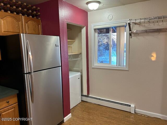 kitchen featuring freestanding refrigerator, a baseboard radiator, washer / clothes dryer, light wood-type flooring, and brown cabinetry