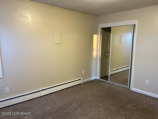 unfurnished bedroom featuring a baseboard heating unit, dark colored carpet, a closet, and a textured ceiling