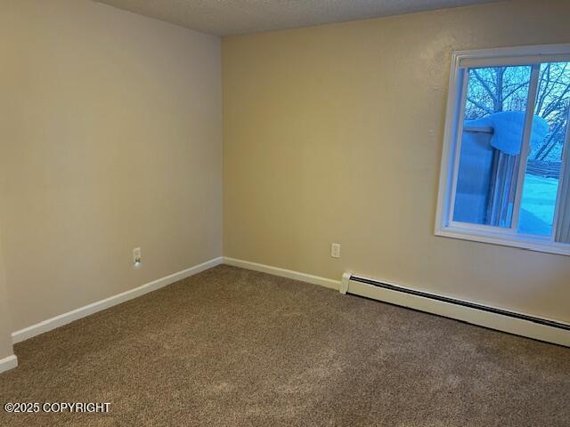 empty room featuring a baseboard heating unit, dark colored carpet, and baseboards