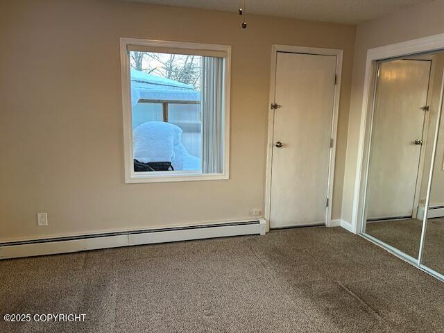 unfurnished bedroom featuring carpet floors, a baseboard heating unit, and a closet