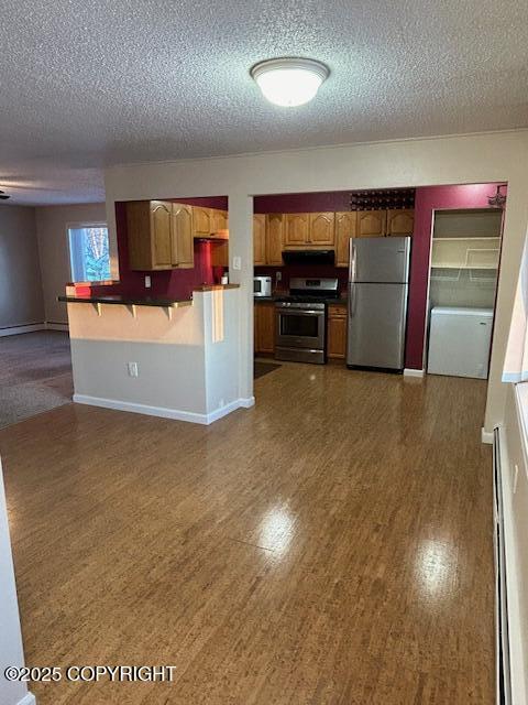 kitchen with stainless steel appliances, dark countertops, baseboards, a textured ceiling, and brown cabinetry