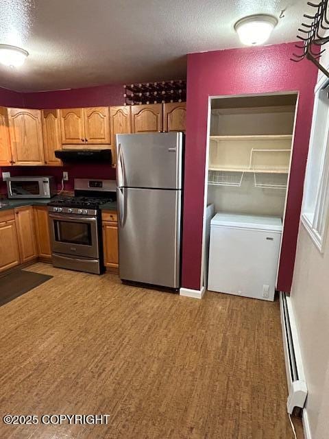 kitchen featuring stainless steel appliances, a textured ceiling, ventilation hood, light wood finished floors, and dark countertops