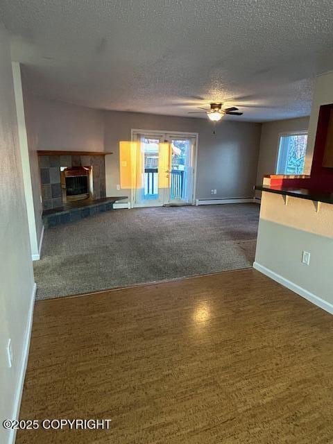 unfurnished living room with dark carpet, a textured ceiling, baseboards, a baseboard radiator, and plenty of natural light