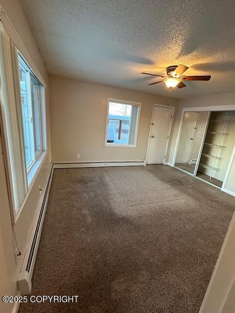 empty room with a textured ceiling, carpet, a ceiling fan, baseboards, and baseboard heating