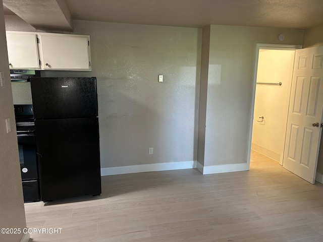 kitchen featuring freestanding refrigerator, ventilation hood, light wood finished floors, white cabinets, and baseboards