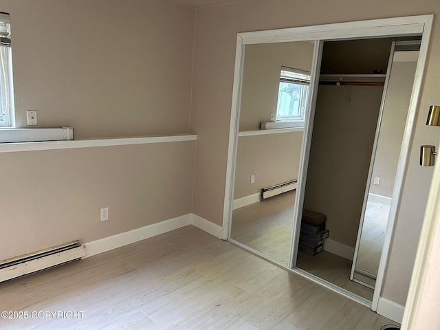 unfurnished bedroom with a closet, wood finished floors, baseboard heating, and baseboards