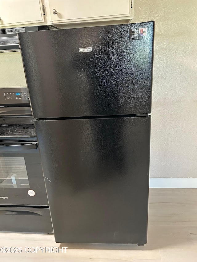 kitchen view of freestanding refrigerator, baseboards, range with electric stovetop, and white cabinetry