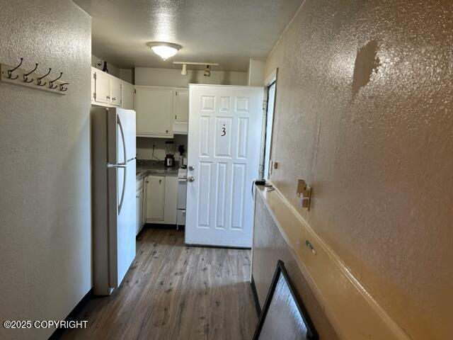 kitchen with white appliances, dark wood finished floors, a textured wall, and white cabinetry