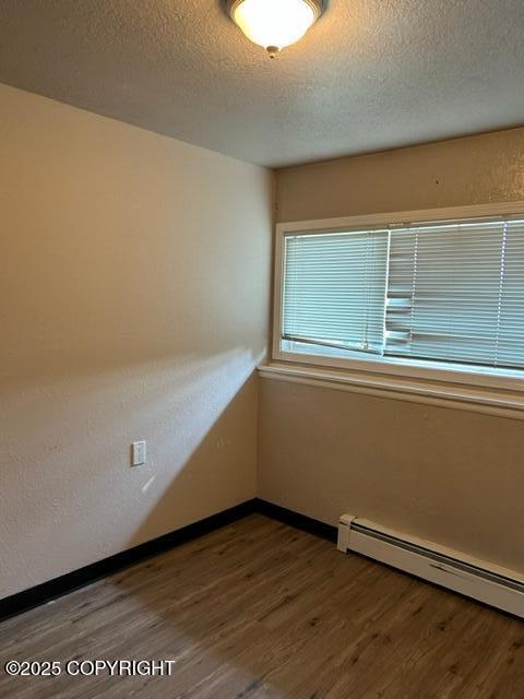 spare room with wood finished floors, a baseboard heating unit, a textured ceiling, and baseboards