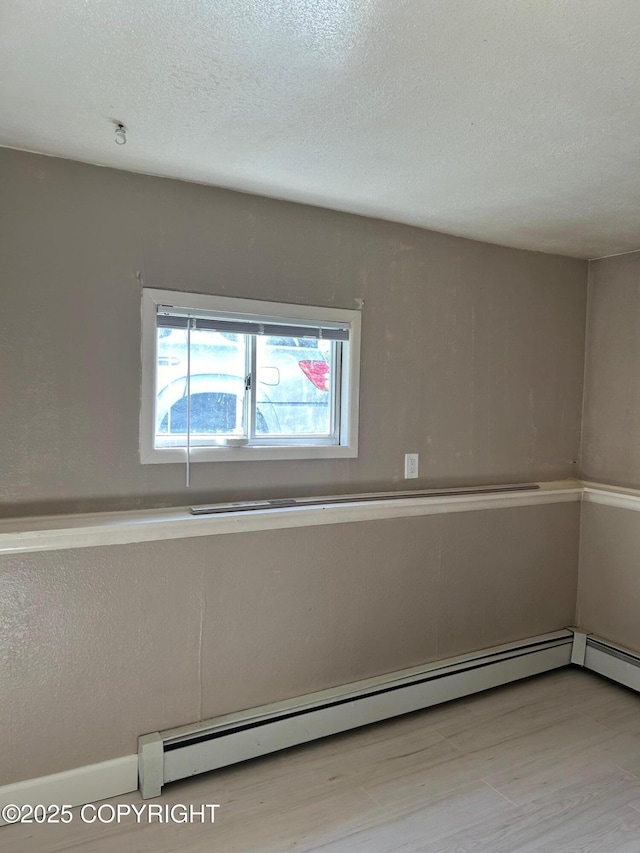 empty room featuring baseboard heating, wood finished floors, and a textured ceiling