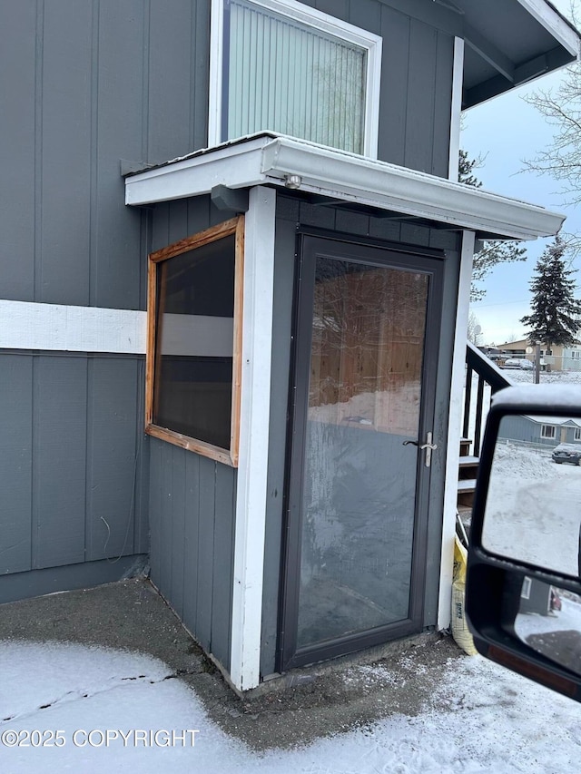snow covered property entrance featuring board and batten siding