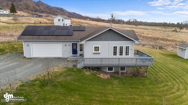 view of front of property with roof with shingles, an attached garage, a front yard, roof mounted solar panels, and driveway