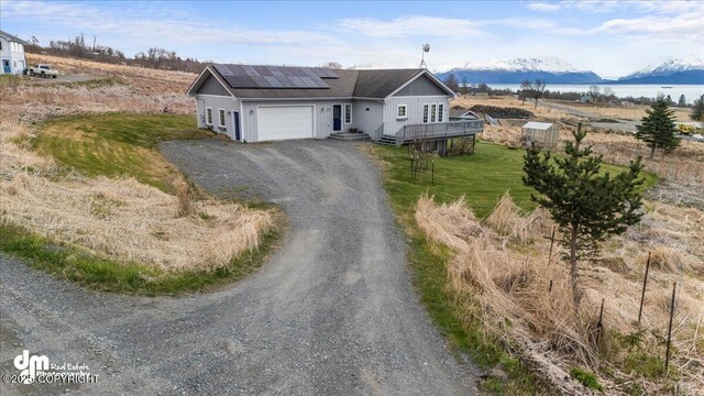 view of front of property with a garage, dirt driveway, roof mounted solar panels, and a water and mountain view