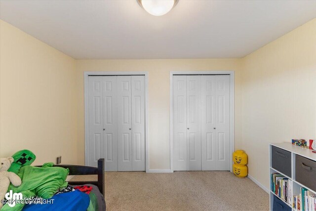 bedroom with baseboards, two closets, and light colored carpet