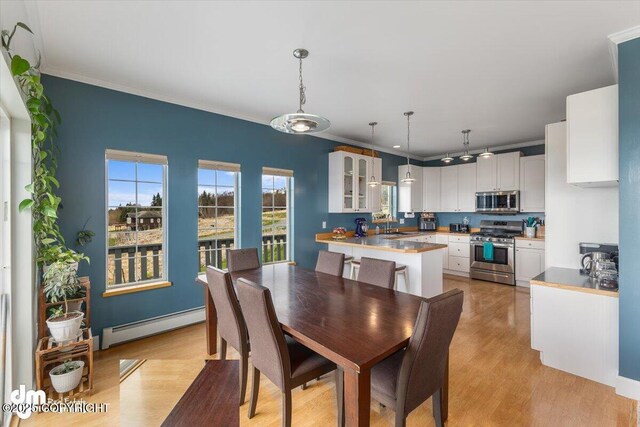 dining room with ornamental molding, a baseboard heating unit, and light wood finished floors
