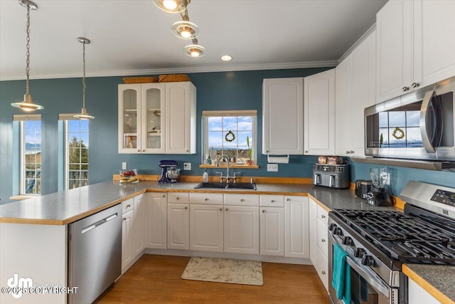 kitchen with a peninsula, glass insert cabinets, light wood-type flooring, a sink, and appliances with stainless steel finishes