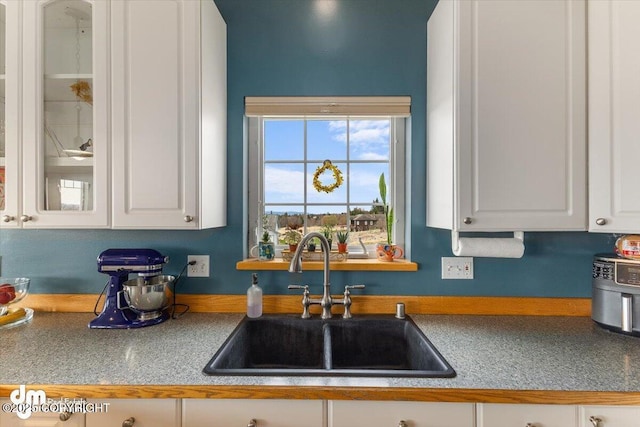 kitchen with a sink, white cabinetry, and glass insert cabinets