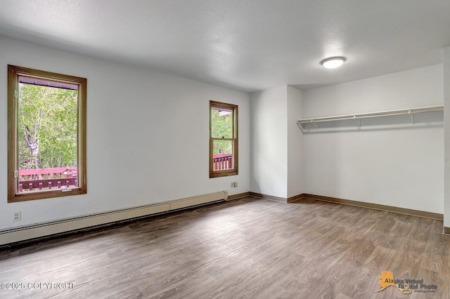 5900 E Liberty Ct, Wasilla, AK 99654 - unfurnished bedroom with multiple windows, baseboard heating, wood finished floors, baseboards, and a textured ceiling