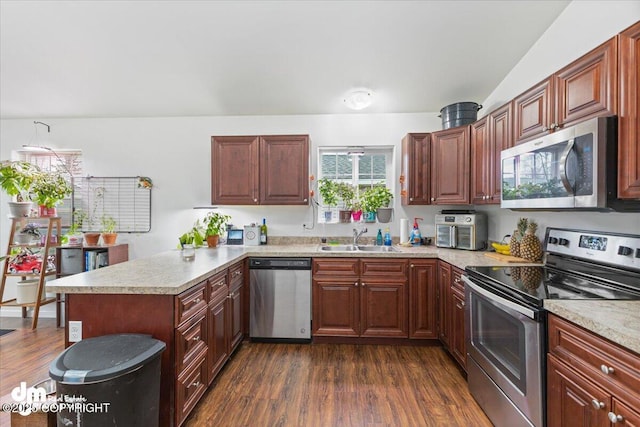 kitchen with a sink, dark wood-style flooring, appliances with stainless steel finishes, and a peninsula