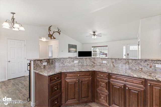 kitchen featuring light stone counters, light wood finished floors, ceiling fan with notable chandelier, decorative light fixtures, and lofted ceiling