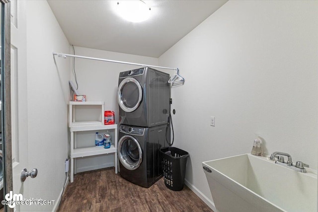 clothes washing area featuring laundry area, stacked washer / drying machine, a sink, baseboards, and dark wood-type flooring