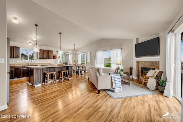 13050 Curry Ridge Cir, Eagle River, AK 99577 - living room featuring vaulted ceiling, light wood-type flooring, a tiled fireplace, a chandelier, and baseboards