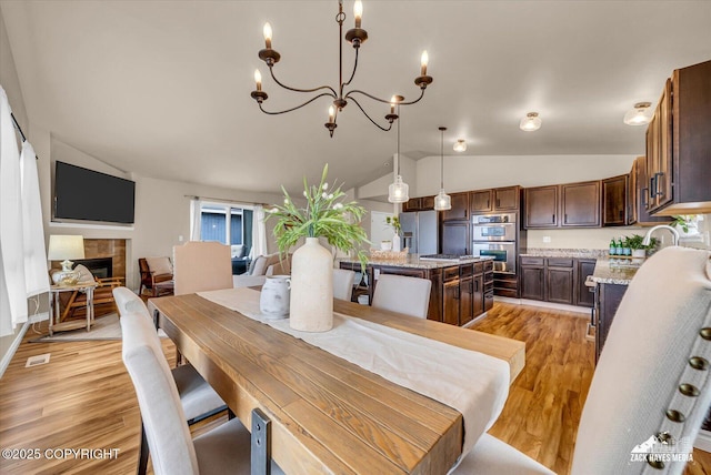 13050 Curry Ridge Cir, Eagle River, AK 99577 - dining space featuring lofted ceiling, light wood-style flooring, a chandelier, and a fireplace