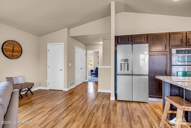 13050 Curry Ridge Cir, Eagle River, AK 99577 - kitchen with stainless steel appliances, lofted ceiling, light wood-style floors, dark brown cabinets, and light stone counters