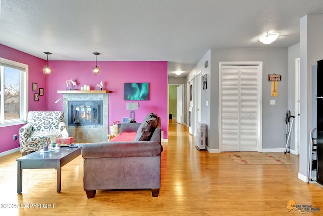 living room featuring a tiled fireplace, baseboards, and light wood finished floors
