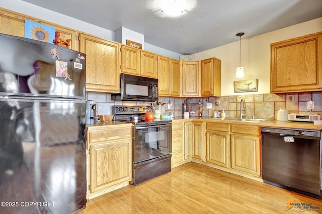 kitchen with a sink, light wood finished floors, light countertops, backsplash, and black appliances