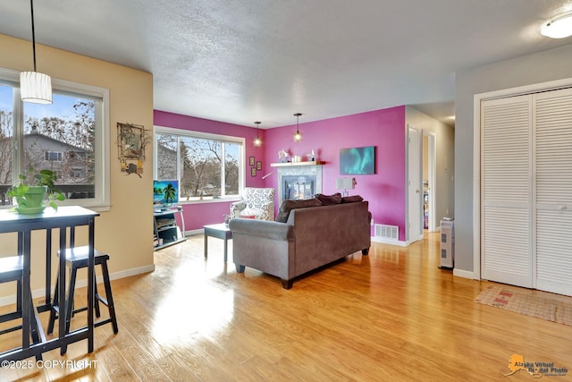 living area with a glass covered fireplace, baseboards, light wood-style flooring, and visible vents